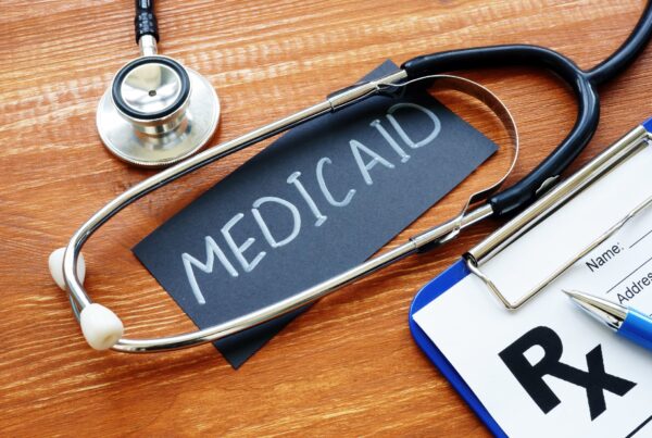 A stethescope ontop of a piece of black paper that says medicaid next to a clipboard that says RX