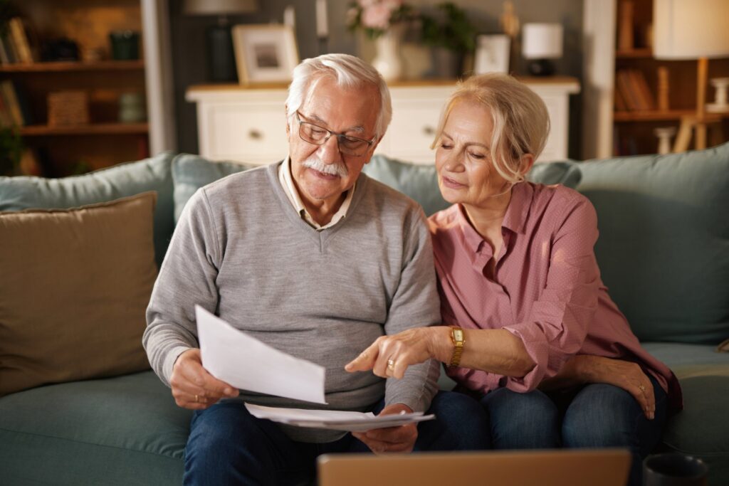 elderly couple sitting on a couch holding paperwork