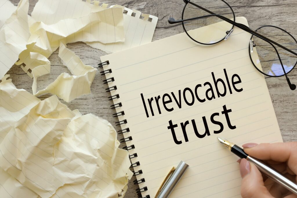 A notebook that says irrevocable trust next to a pair of glasses and crumbled up paper