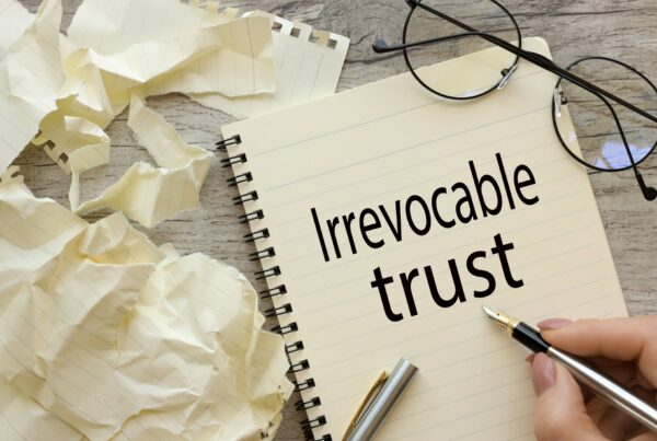 A notebook that says irrevocable trust next to a pair of glasses and crumbled up paper