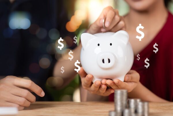 A person in a red shirt holding a piggy bank while another person puts money inside