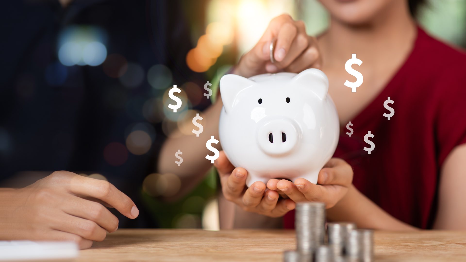 A person in a red shirt holding a piggy bank while another person puts money inside