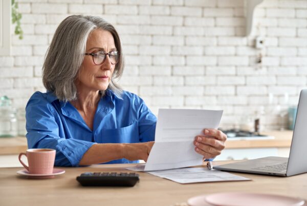 Older woman in a blue shirt sitting at a desk going over paperwork