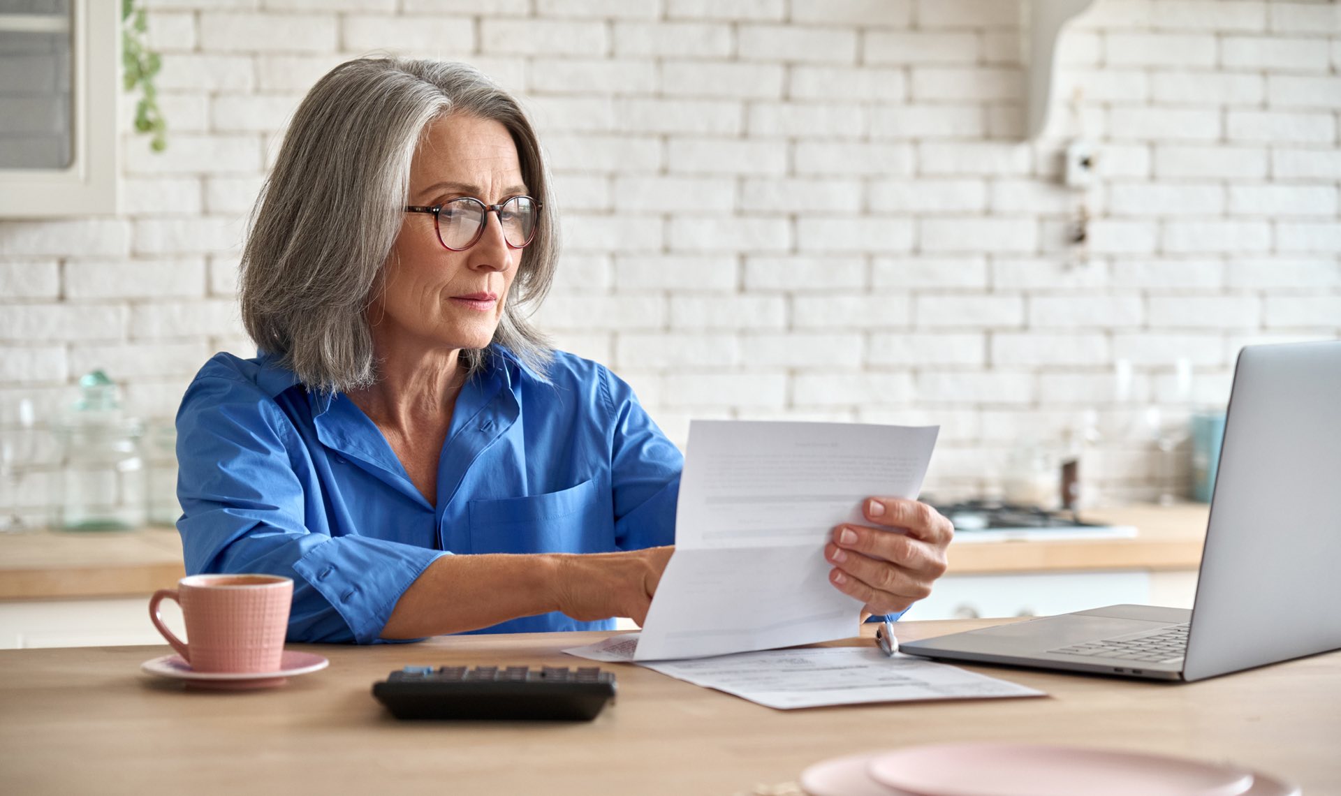 Older woman in a blue shirt sitting at a desk going over paperwork