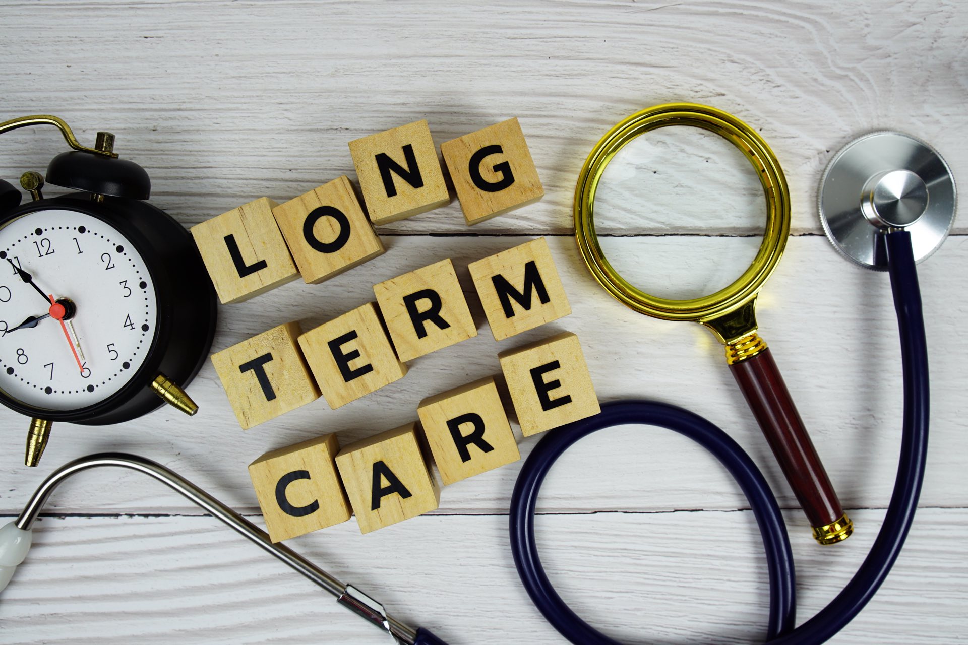 Long term care with wooden boxes next to a stethoscope, a magnifying glass and a clock